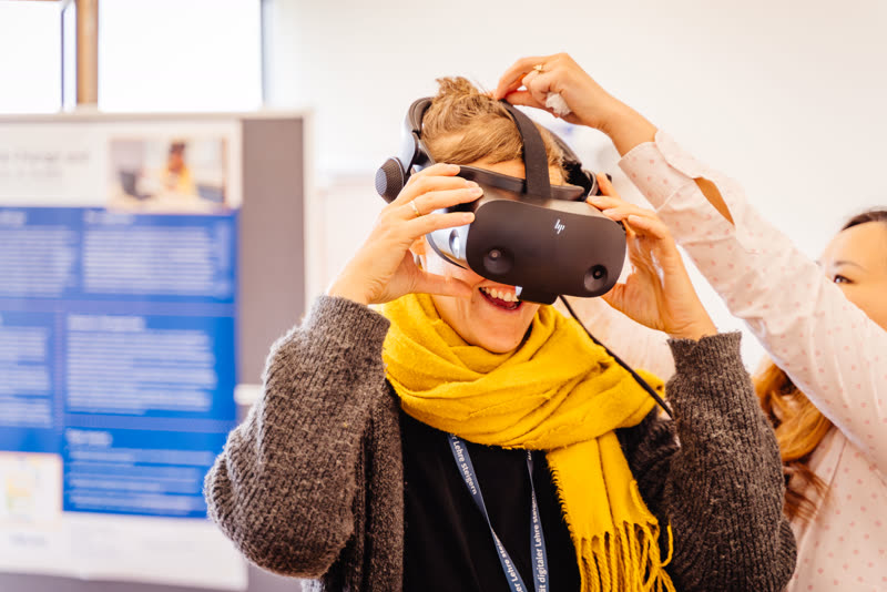 Einer Person wird lachend ein VR-Headset aufgesetzt
