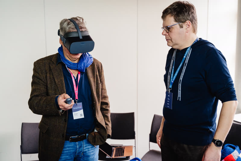 Ein Teilnehmer testet ein VR-Headset, eine Kollegin schaut zu
